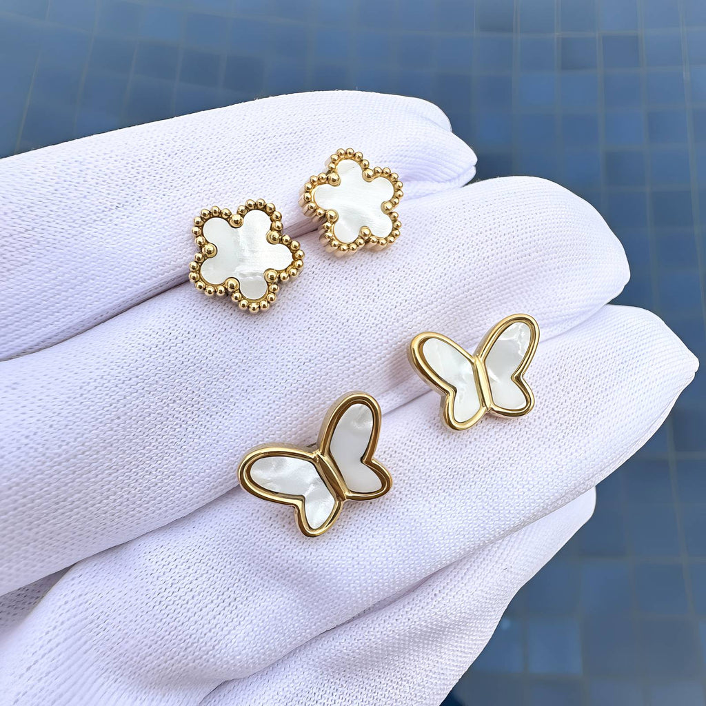 Gold and white butterfly-shaped earrings on a white cloth with a blue tiled background