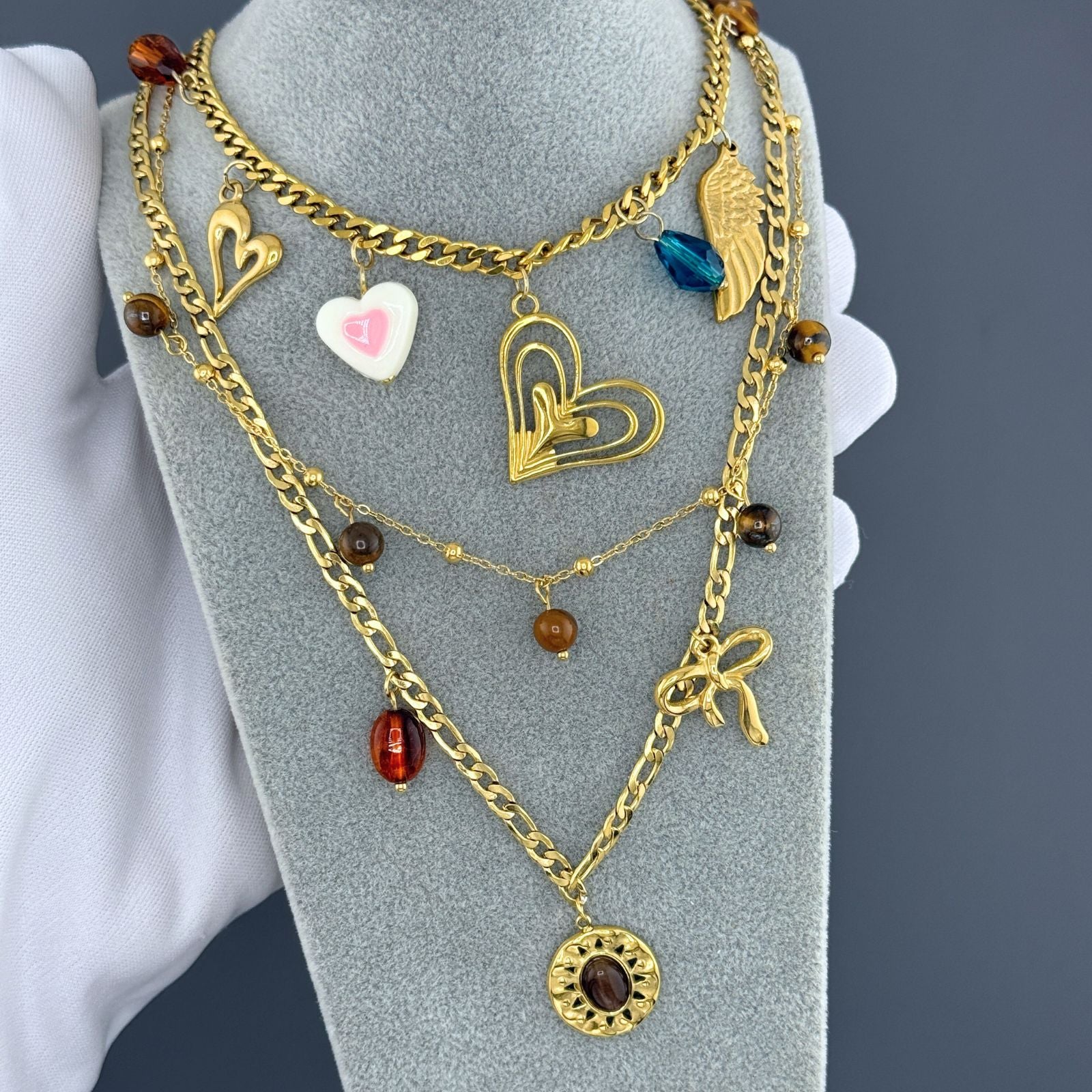 Layered Gold heart charm necklace featuring an angel wing charm, blue crystal accent, and layered heart pendant crafted from waterproof hypoallergenic stainless steel.
