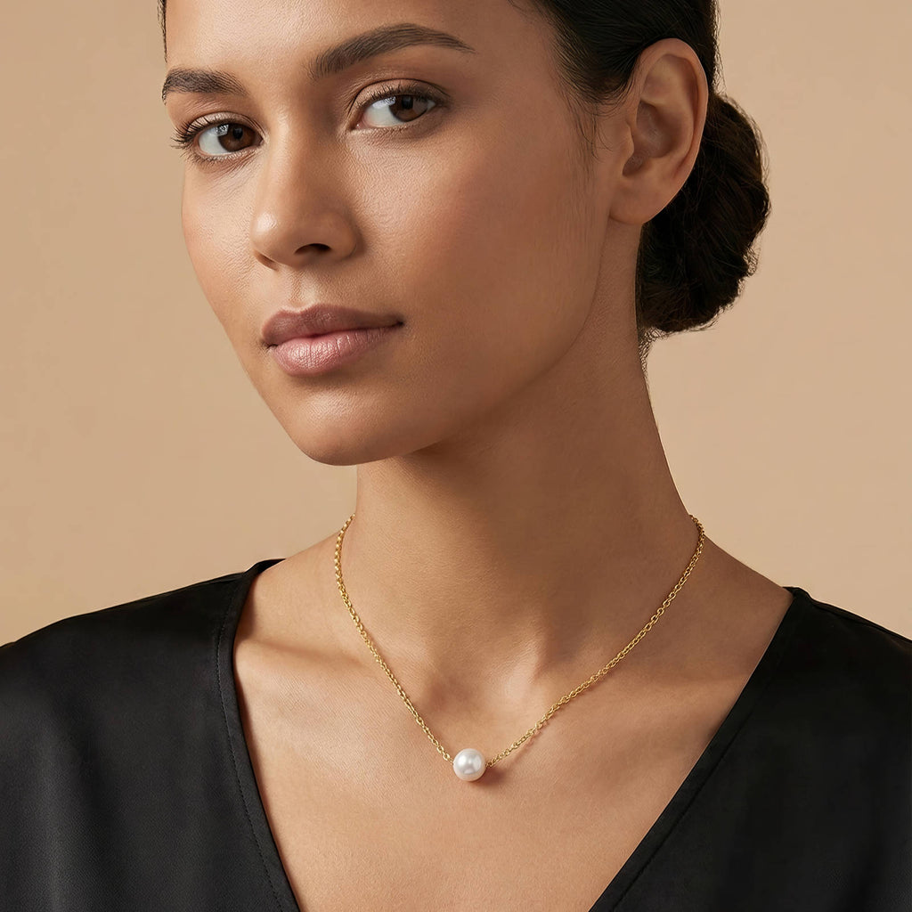 Woman wearing a gold necklace with a pearl pendant against a beige background