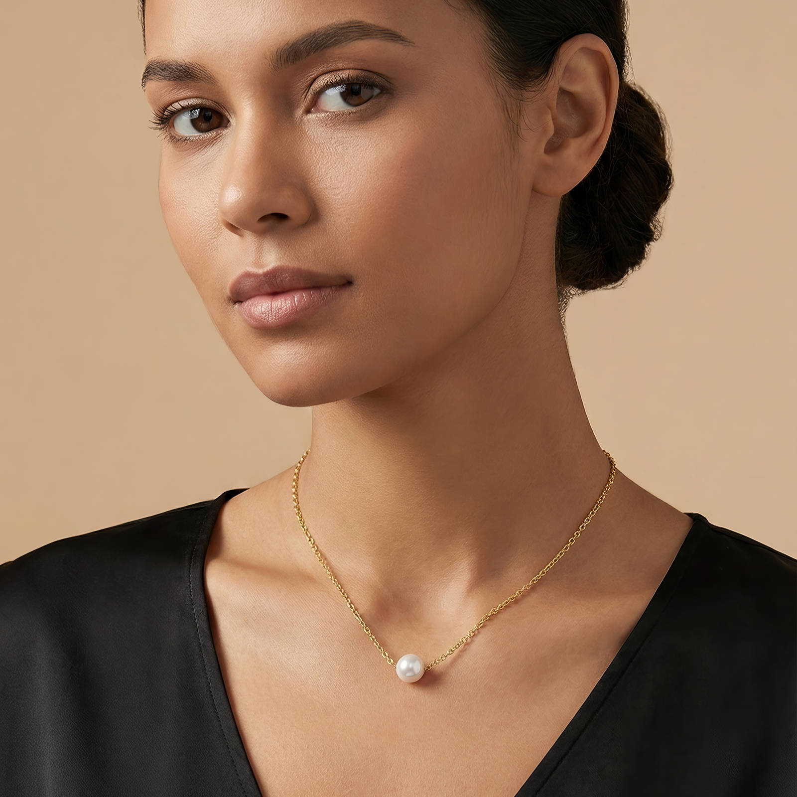 Woman wearing a gold necklace with a pearl pendant against a beige background