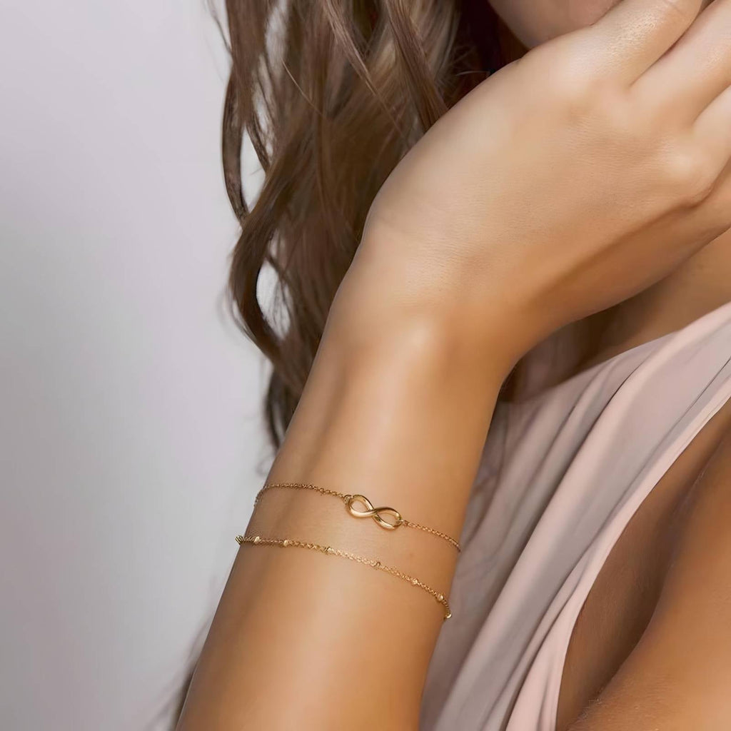 Close-up of 18K gold plated stainless steel infinity bracelet featuring a delicate double-chain design and adjustable fit.