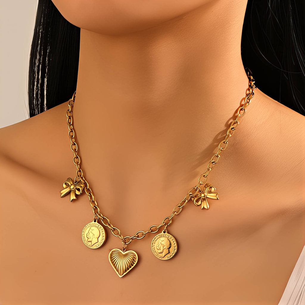 Gold charm necklace featuring a heart pendant, bow accents, and vintage coin charms crafted from waterproof hypoallergenic stainless steel.
